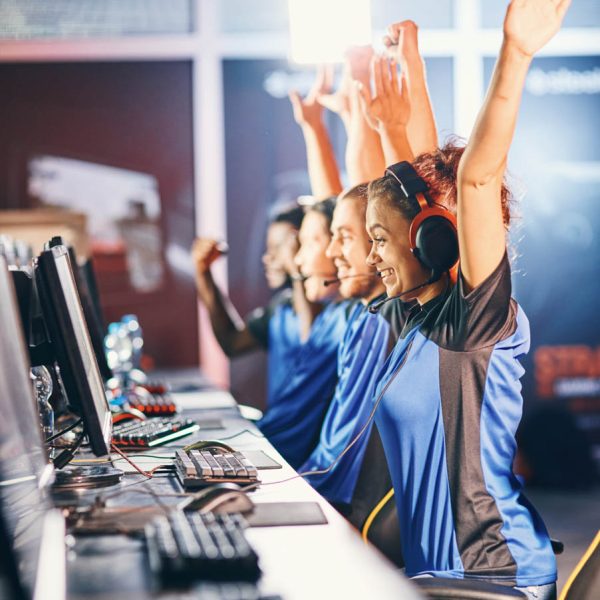 Winning. Young multiracial team of happy professional cyber sport gamers celebrating success, raising hands up while participating in eSports tournament, playing online video games